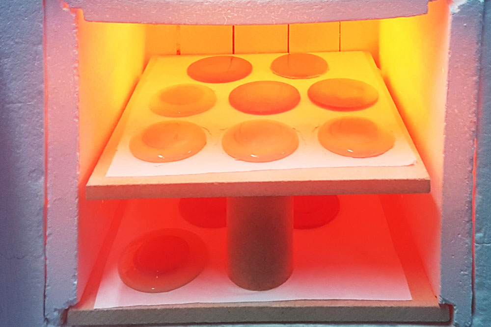 Glass kiln interior showing molten glass pieces being fired at high temperature during manufacturing process