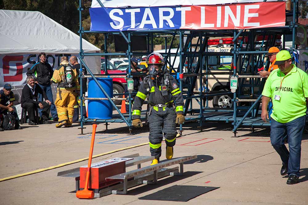 Firefighter in full protective gear navigating obstacle course during timed rescue challenge at SAESI competition