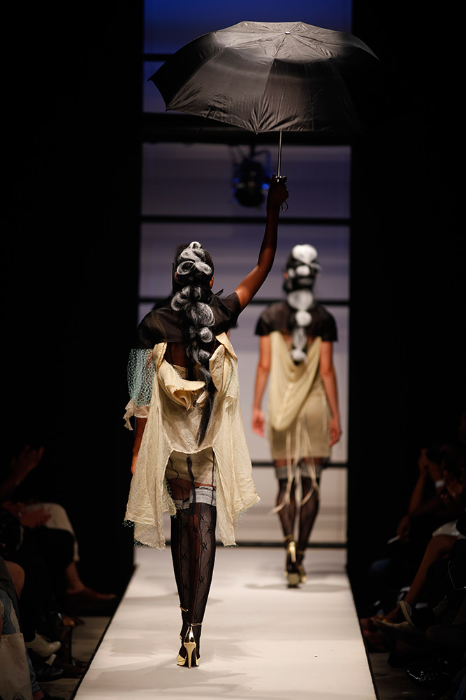 Dramatic fashion runway photography with model holding umbrella in theatrical presentation showing sculptural styling