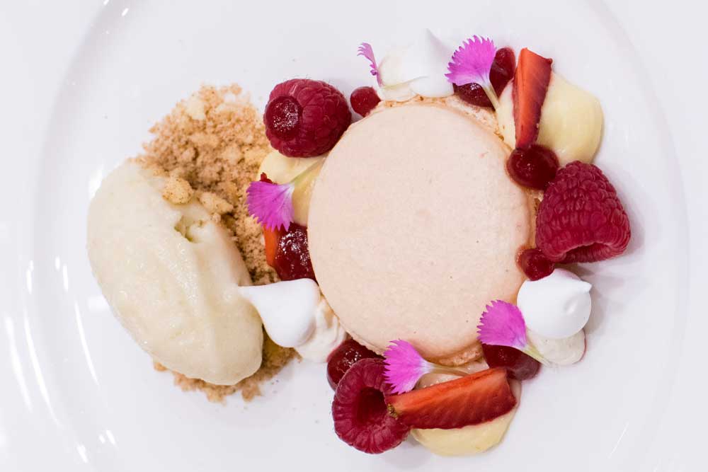 Fine dining dessert with panna cotta, fresh berries, edible flowers and ice cream on white plate