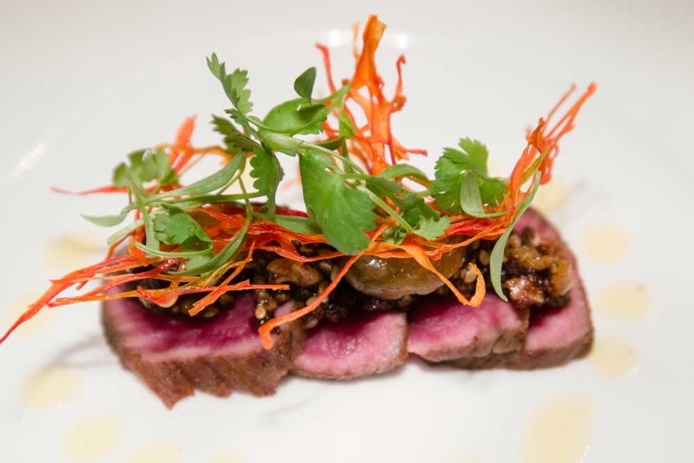 Professional food photography of sliced seared meat with Asian-style garnish and microgreens