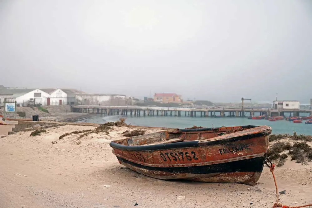 Rustic boat and wooden jetty on the misty shoreline of Port Nolloth